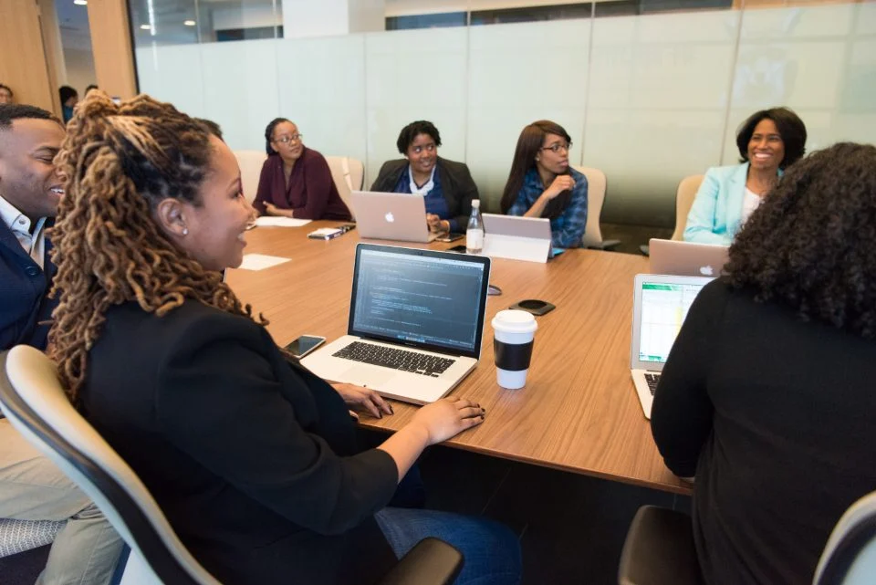 Equipe reunida numa mesa de reunião com notebooks abertos, um deles com código na tela