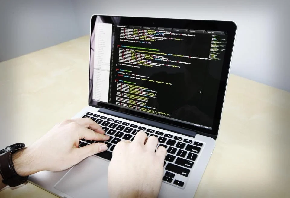Mãos digitando num notebook com código na tela