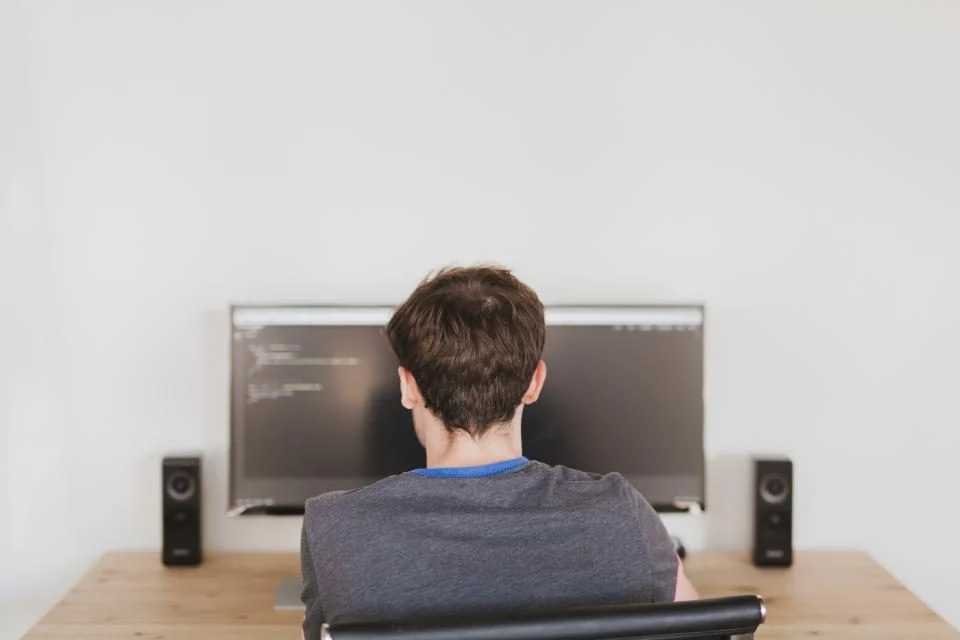 Homem de costas trabalhando num computador com código na tela