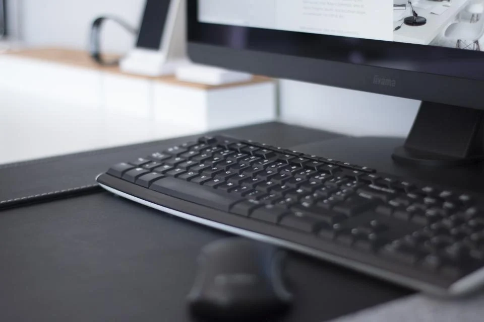 Teclado e monitor de um computador de mesa sobre uma mesa escura
